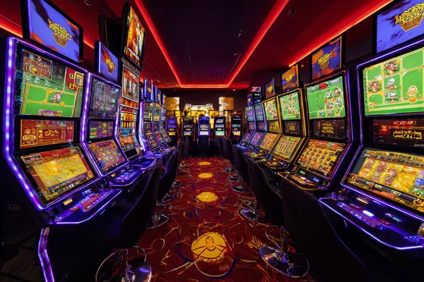 A woman smiling by bright slot machines showing lucky symbols, showcasing the exciting slot offerings at K677.